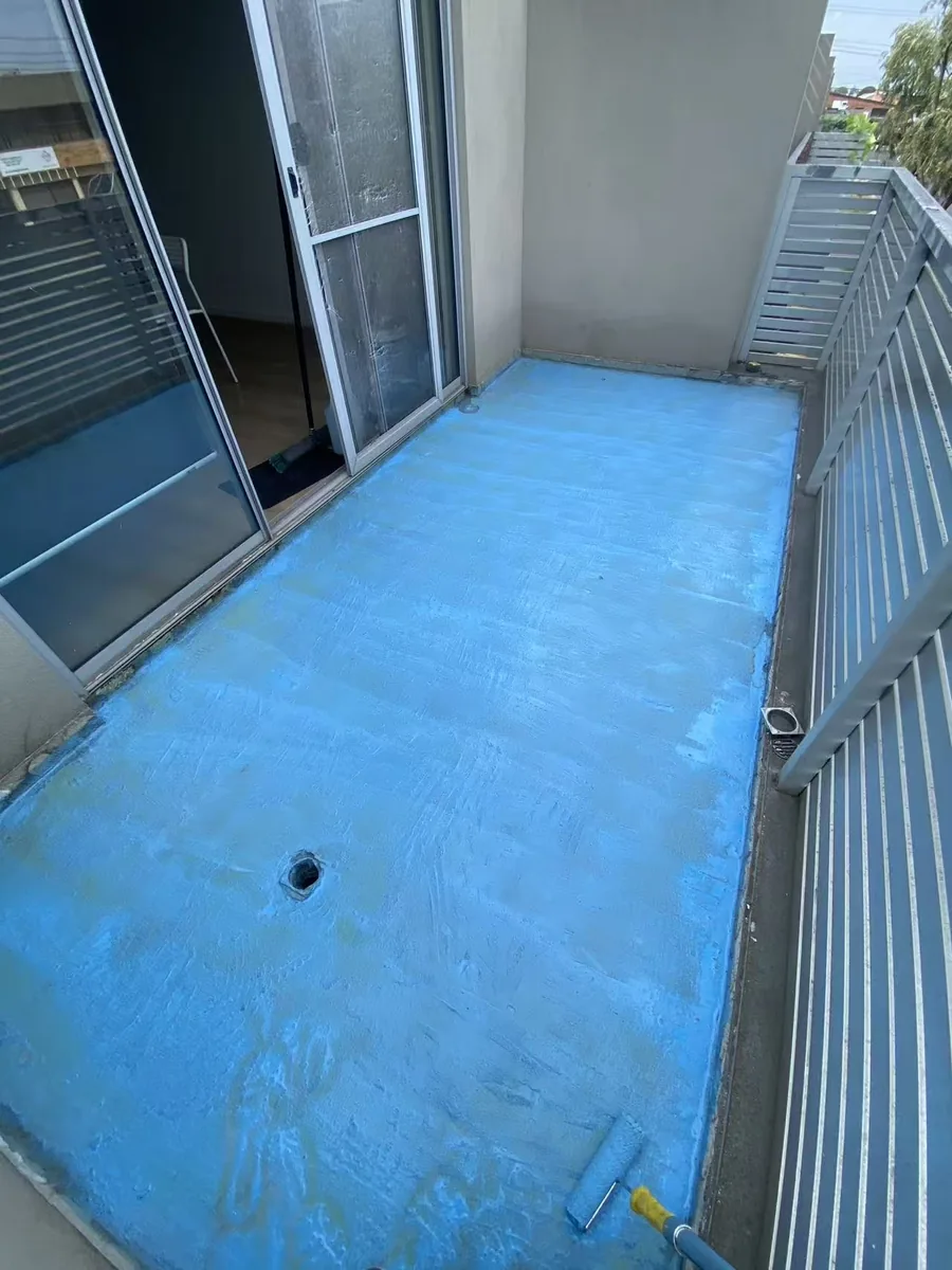 Blue waterproofing membrane being rolled across a balcony floor