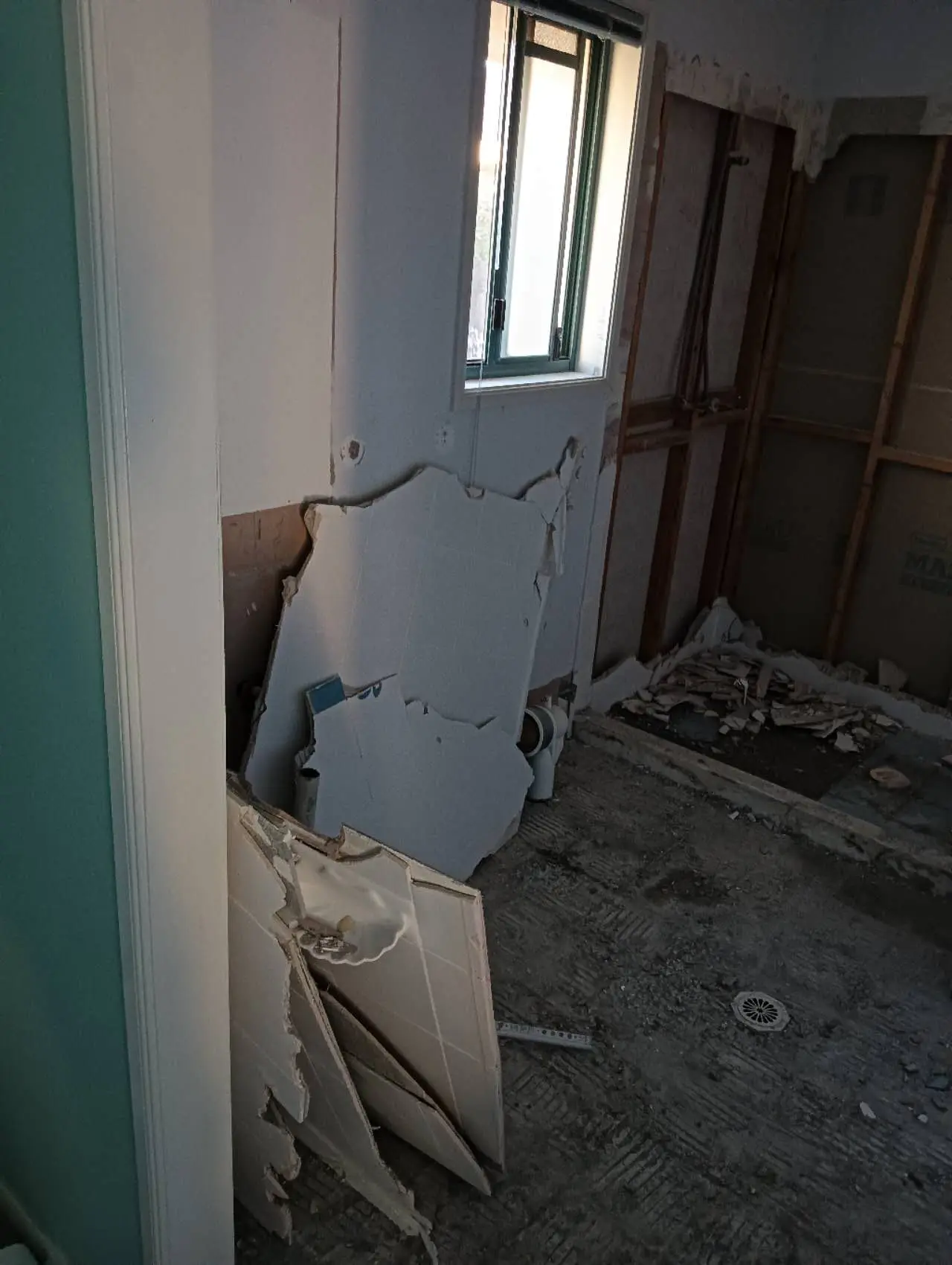 Bathroom demolition and strip-out exposing wall framing and floor drainage