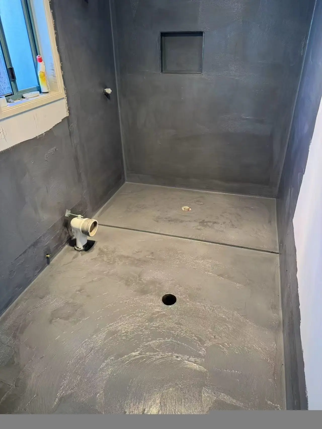 Grey waterproofing membrane applied across bathroom walls and floor