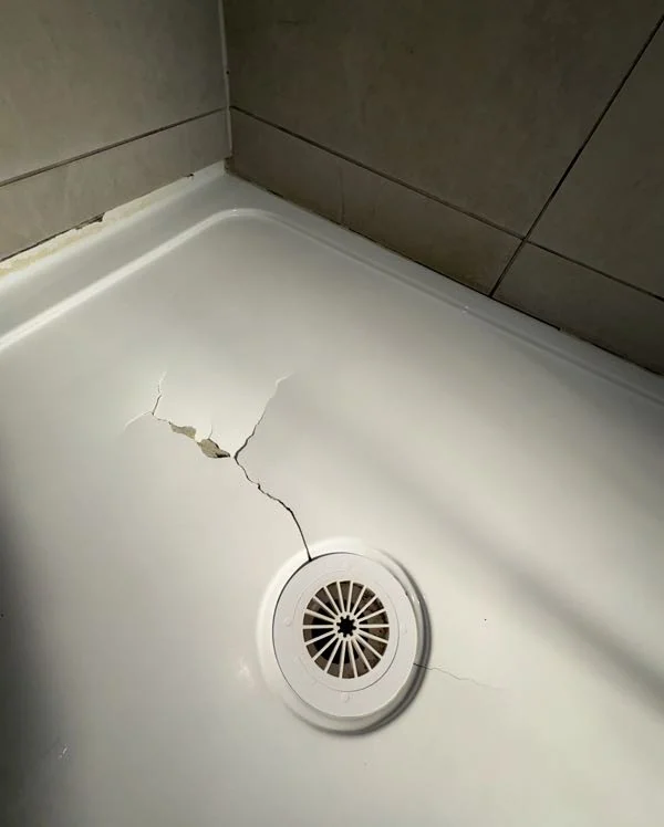 Cracked white shower base beside the round floor waste before repair
